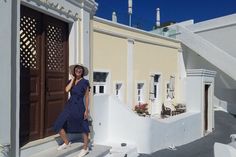 a woman in a dress and hat standing on steps next to a building with doors