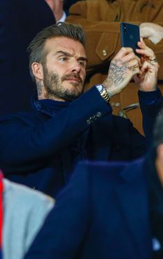 a man taking a selfie with his cell phone at a sporting event while sitting in the stands