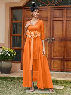 a woman standing in front of a door wearing an orange dress with a bow at the waist