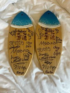 two wooden surfboards with handwritten names are on a white sheet and one has a blue fin