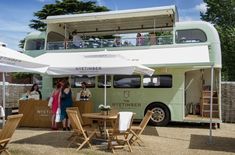 a double decker bus parked next to a table with chairs and umbrellas on it