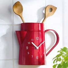 a red watering can with wooden spoons in it and a clock on the wall