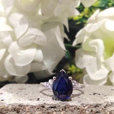 a blue sapphire and diamond ring sitting on top of a stone slab next to white flowers