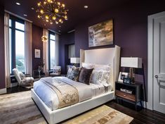 a bedroom with purple walls and white bedding in the center is lit by a chandelier