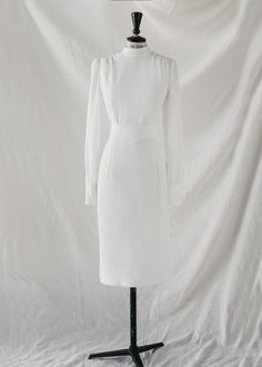 Wedding dress made UPON REQUEST (*) from the Ready to Love collection.



Wedding dress made to order.

midi cut

Long sleeves with closed cuffs and buttons.

Neck to the box.

Straight skirt.


Back with invisible zip and covered button placket. 

Belted framed waist.

Made in white crepe.












Size

US

UK



Bust

(cm)*






Waist

(cm)*






Hip

(cm)*






Back 

(cm)*














XS

34-36

6-8

84

64

90

35






S

36-38

8-10

88

68

94

39






m

38-40

10-12

92 

72

98

43






L

40-42

12-14

96

76

102

47






XL

42-44

14-16

100

80

106

51
















 *GENERAL MEASUREMENTS: some fabrics are more flexible than others. Please keep this in mind when measuring yourself.

To keep your CHERUBINA dress like the first day, we recommend a professional White Wedding Dress With Structured Shoulders, Classic Tea Length Dress With Fitted Bodice, Classic Dress With Fitted Bodice, Tea Length, Semi-formal Fitted Dress With Pleated Sleeves, Classic Tea-length Dress With Fitted Bodice, Fitted Dress With Pleated Sleeves For Semi-formal Occasions, Fitted Dress With Pleated Sleeves For Semi-formal Events, Formal Long Sleeve Tea Length Dress, White Formal Dress With Structured Shoulders