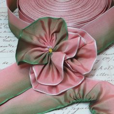 pink satin ribbon with green trim and flower on white table top next to old letter