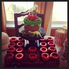 a table topped with lots of red cupcakes next to a cake on top of a plate