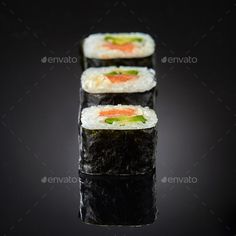 three sushi rolls with different toppings on top of each other, sitting on a black surface