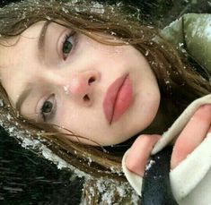 a woman is holding something in her hand while she looks at the camera with snow all over her face