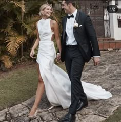 a man and woman in formal wear walking down a stone path holding each other's hand