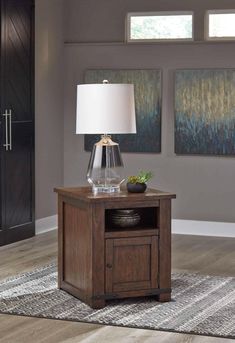 a table with a lamp on it in front of two paintings and a rug underneath