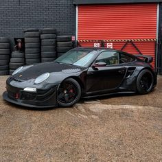 a black sports car parked in front of a red garage door next to some tires