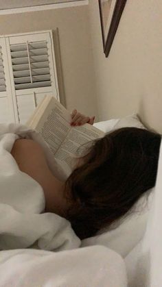 a woman laying in bed reading a book