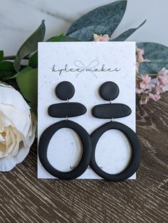 the black earrings are on display next to a white flower and a card that says style makes