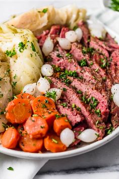 a white bowl filled with meat, potatoes and carrots on top of a table