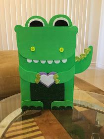 a paper cut out of a green crocodile holding a heart on top of a glass table