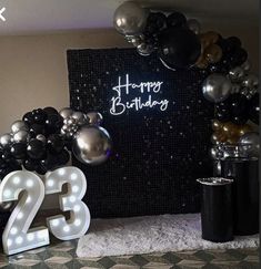 a birthday party with balloons and lights on the wall, black and silver decorations in front of it