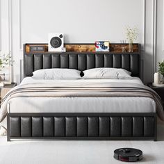 a bed with white sheets and black leather headboard in a large room next to a speaker