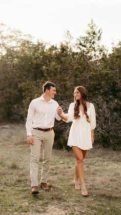 a man and woman holding hands walking through the grass