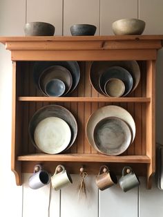 a wooden shelf with bowls and cups on it's sides, hanging from the wall