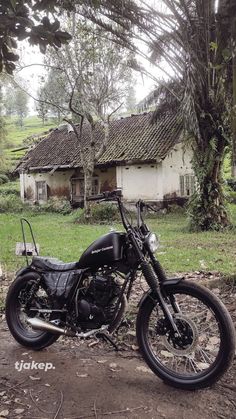 a black motorcycle parked in front of an old house on the side of a dirt road