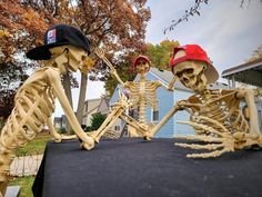 two fake skeletons sitting on top of a table in front of a blue house with trees