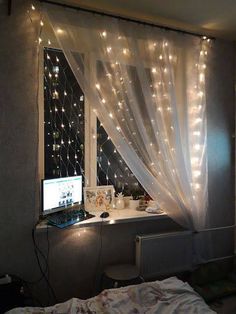 a laptop computer sitting on top of a desk next to a window covered in fairy lights