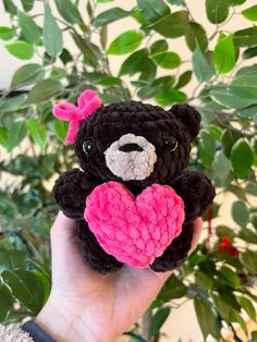 a hand holding a crocheted teddy bear with a heart