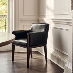 a black leather chair sitting in front of a white wall and window with wooden trim