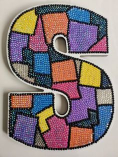 the letter s is made up of multicolored beads and sequins on white background