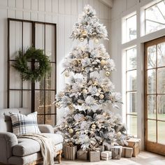 a white christmas tree with gold ornaments and presents in front of an open window at night