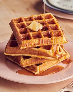 a stack of waffles sitting on top of a pink plate covered in syrup