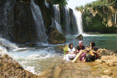 people sitting on rocks in front of a waterfall