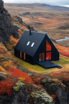 a black house on the side of a mountain with red and yellow trees around it