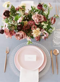 a table setting with pink plates, silverware and floral centerpieces on it