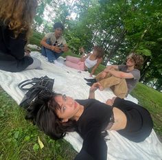 a group of women sitting on top of a blanket in the grass next to trees