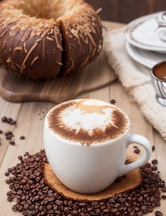 a cappuccino on a wooden table with coffee beans and doughnuts in the background