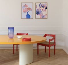 two paintings hang on the wall next to a table with red chairs and a blue vase