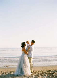 a man and woman standing on top of a sandy beach next to the ocean with their arms around each other