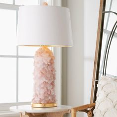 a pink lamp sitting on top of a white table next to a chair and mirror