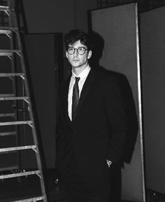 a black and white photo of a man in a suit standing next to a ladder