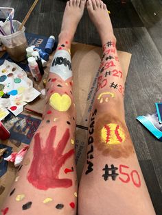 two people with painted arms and legs sitting on the floor in front of paintbrushes