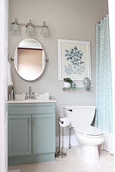 a white toilet sitting next to a sink in a bathroom under a round mirror on the wall