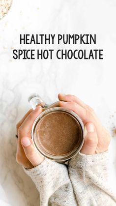 a woman holding a cup of hot chocolate in her hands with the words healthy pumpkin spice hot chocolate