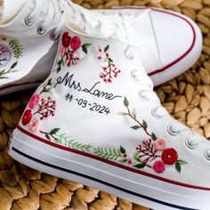 two white shoes with embroidered flowers on them sitting on a woven basket next to each other