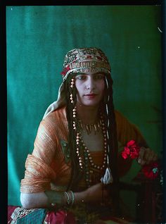 Anonymous - Middle Eastern Woman Holding Flowers, ca. 1910. Middle Eastern Character Inspiration, Middle Eastern People, Middle Eastern Art Women, Persian Flowers, Woman Holding Flowers, Middle Eastern Portrait Photography, Cultural Costumes, Old Arab Art Women