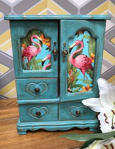 a blue cabinet with pink flamingos painted on the doors and drawers is next to a white flower