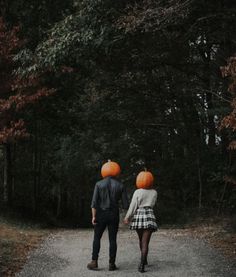 two people walking down a road with pumpkins on their heads and one person holding the other's hand