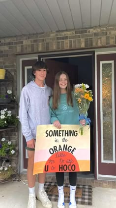 two people standing in front of a door holding a sign that says something in the orange