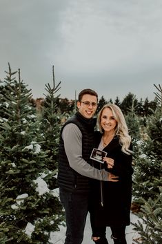 a man and woman standing next to each other in the middle of a christmas tree farm